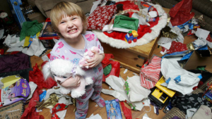 Child smiling in the middle of a messy room after opening presents.