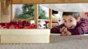 Young boy reaching for a present hidden under a bed.