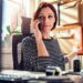 Business woman sitting in front of work computer while talking on the phone.