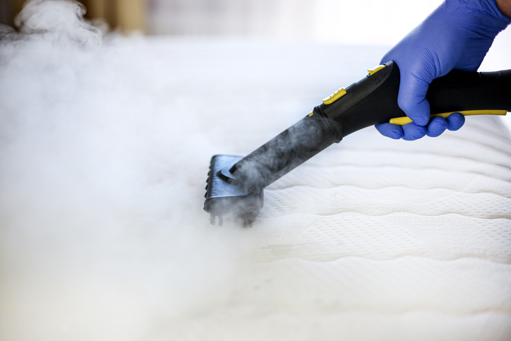 A person steaming a mattress to clean it before placing it in storage.