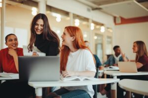 Three women gather around a laptop while looking and smiling at each other