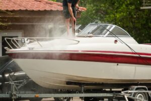 A boat on a trailer with a man power washing the boat to maintain its cleanliness