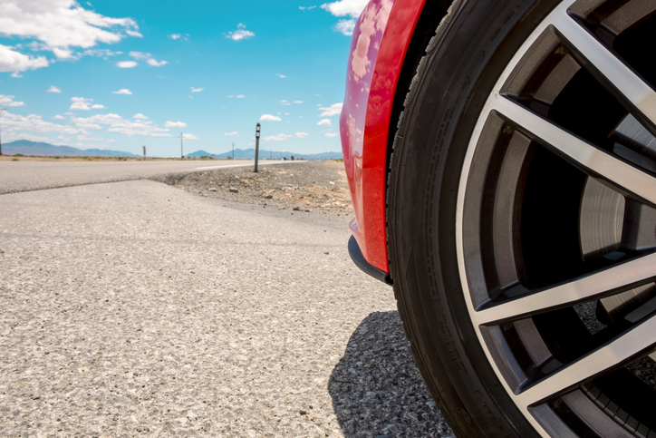 A red car sitting on an asphalt road in the desert on a hot day.