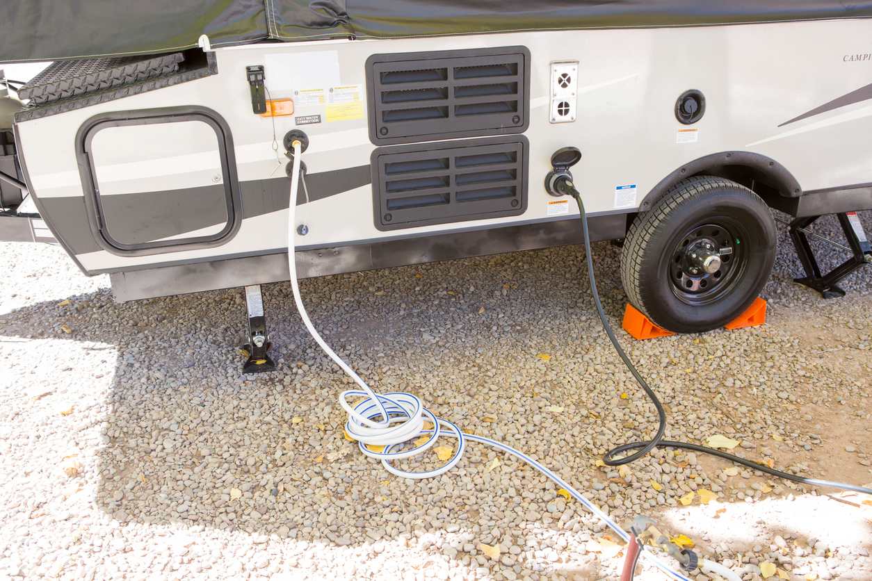 An RV’s water and power hookups are connected at a gravel campsite with hoses and cables neatly in place.