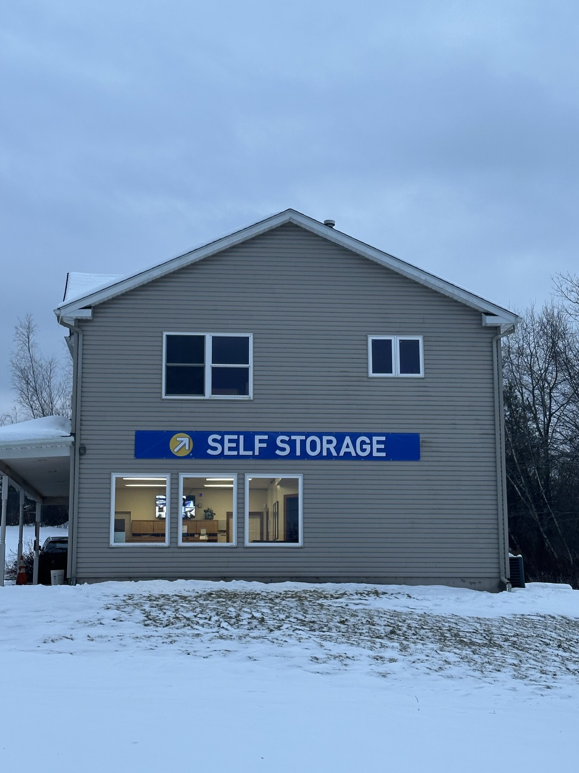 Self storage office building exterior in winter with snow, featuring a blue 'SELF STORAGE' sign.