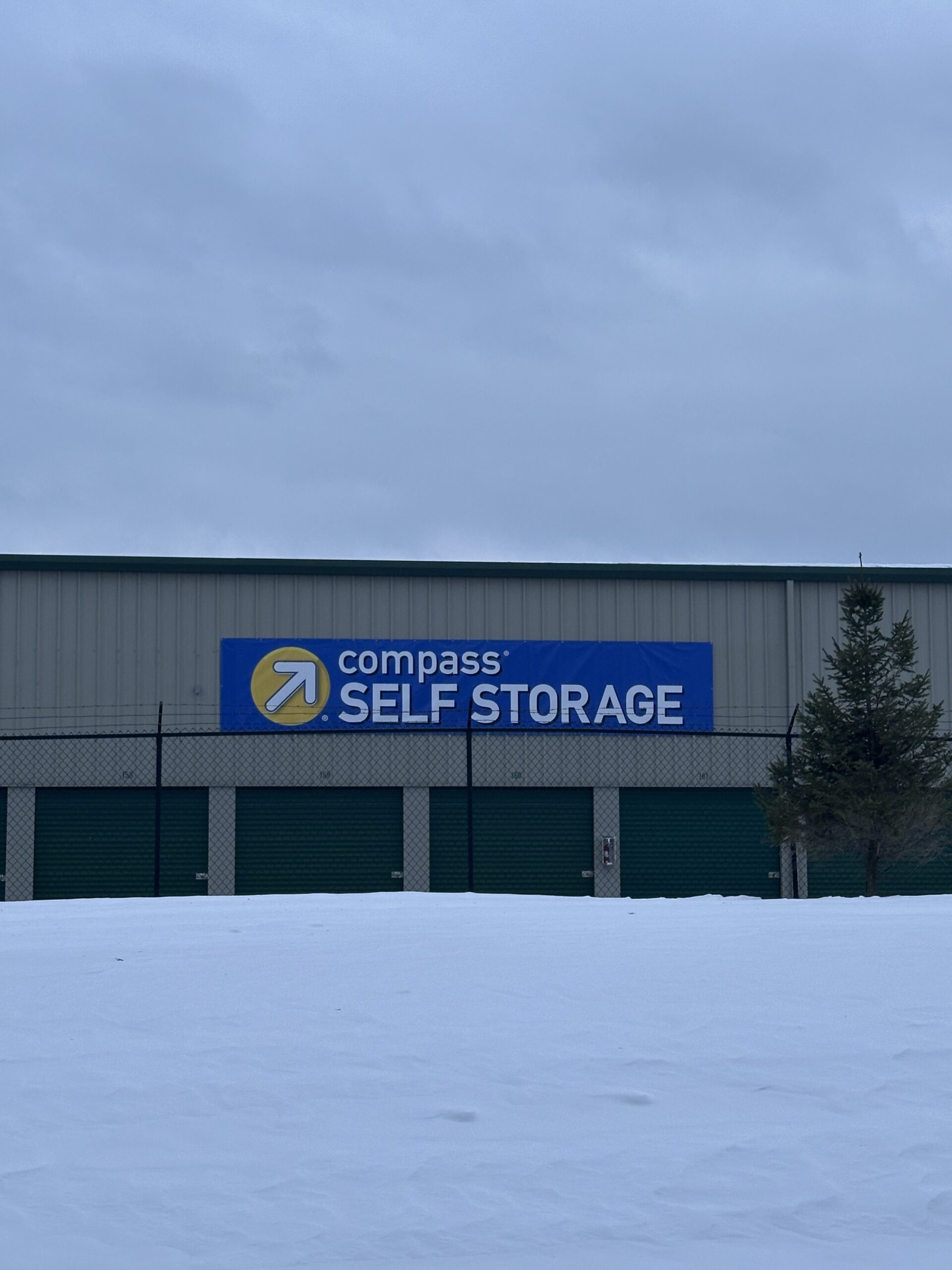 Compass Self Storage building exterior with blue sign, green unit doors, and snowy foreground.