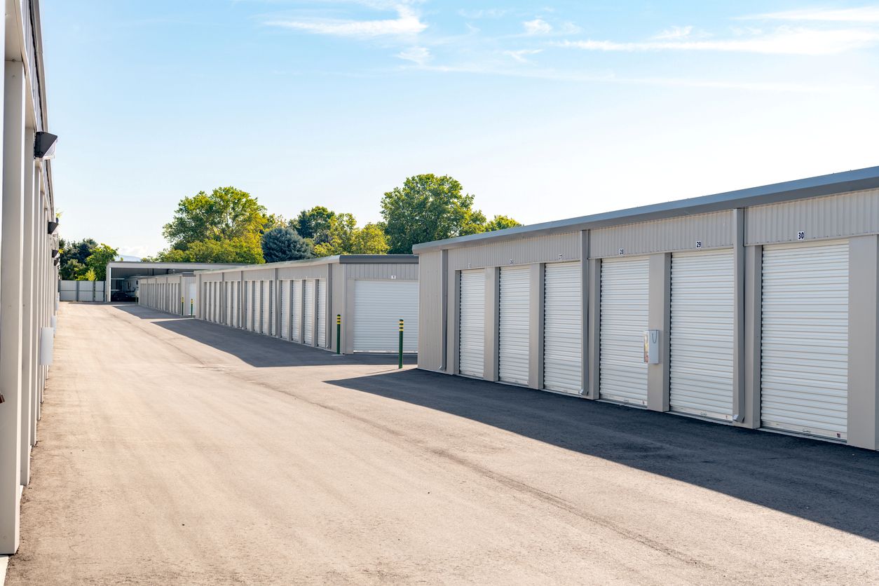 Rows of drive-up storage units with white doors on a sunny day with trees behind.