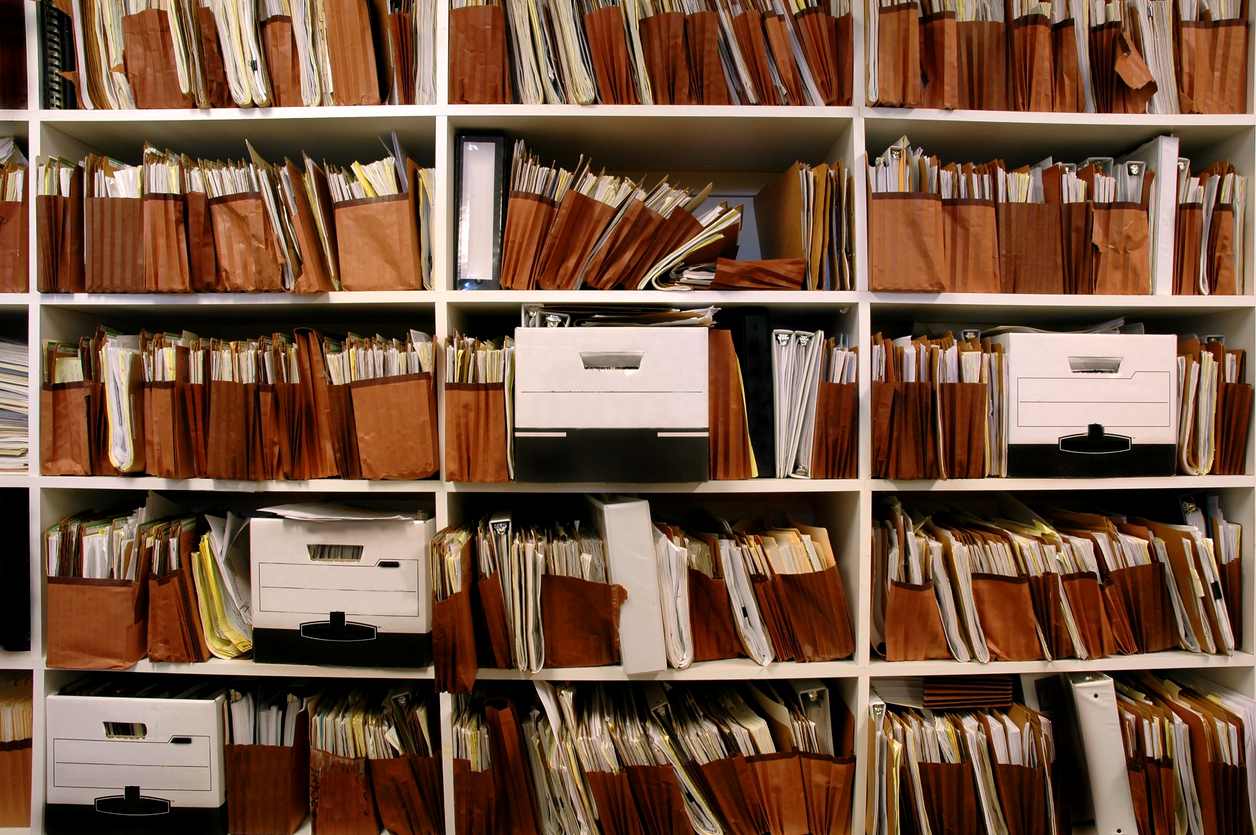 Shelves filled with paper files in brown file holders and white and black document boxes.