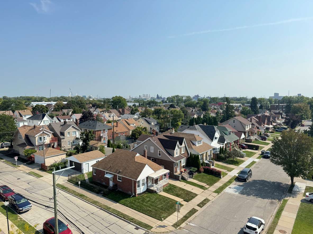 A neighborhood community with streets lined with mid-sized homes, trees, and parked cars