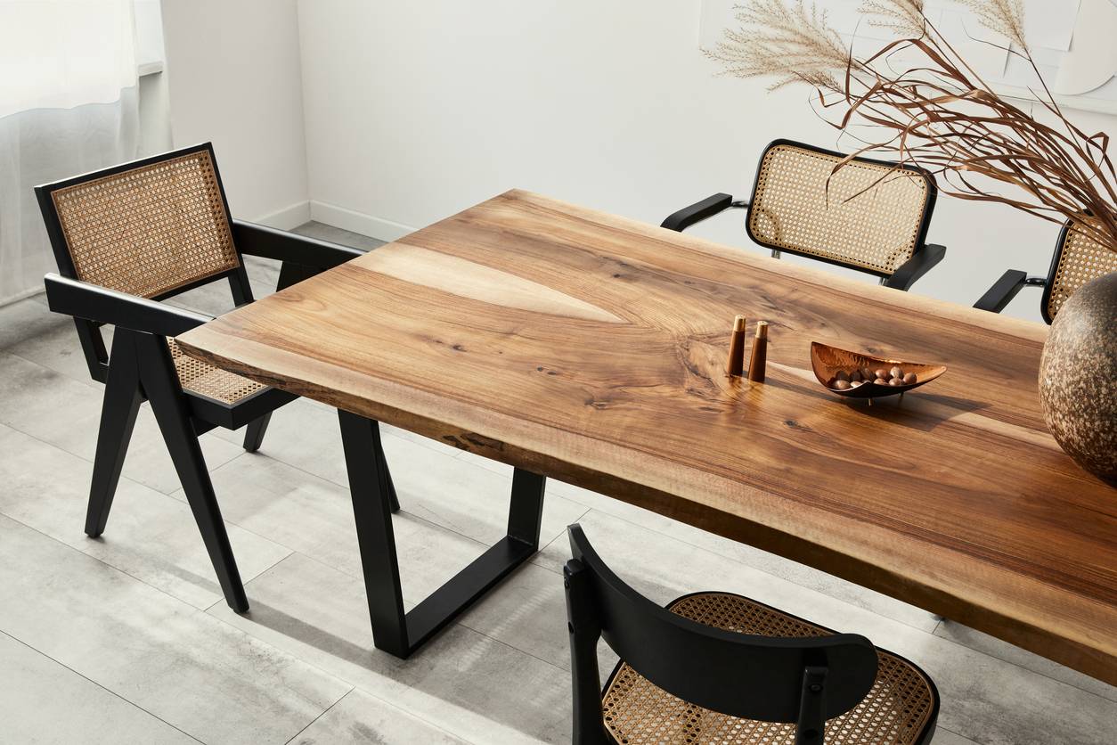 A modern dining room with a large natural wood table, black chairs with cane seats, and minimalist decor