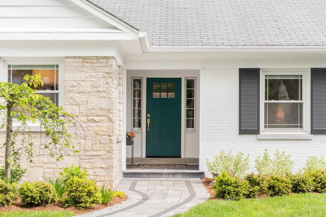 A green front door on a house fitted with white brick and cobblestone exterior walls