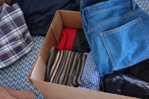 Folded clothes and jeans packed neatly in a cardboard box, ready for seasonal storage and organizing at home.