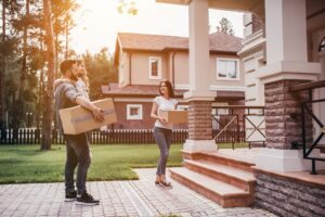 Happy couple is standing near new house with cardboard boxes.
