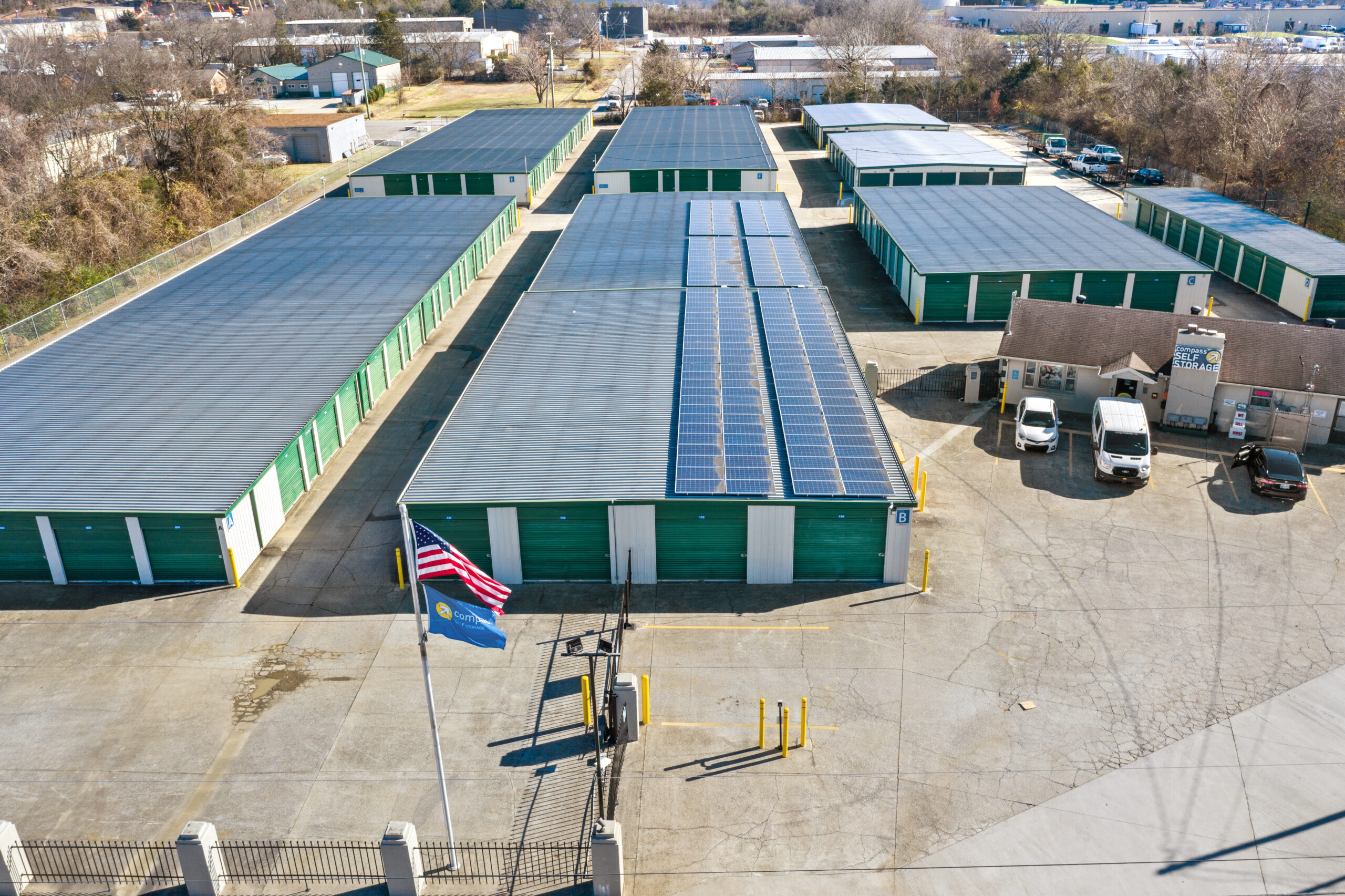 Large self-storage facility with rows of green units, office, US flag, and solar panels on one roof.