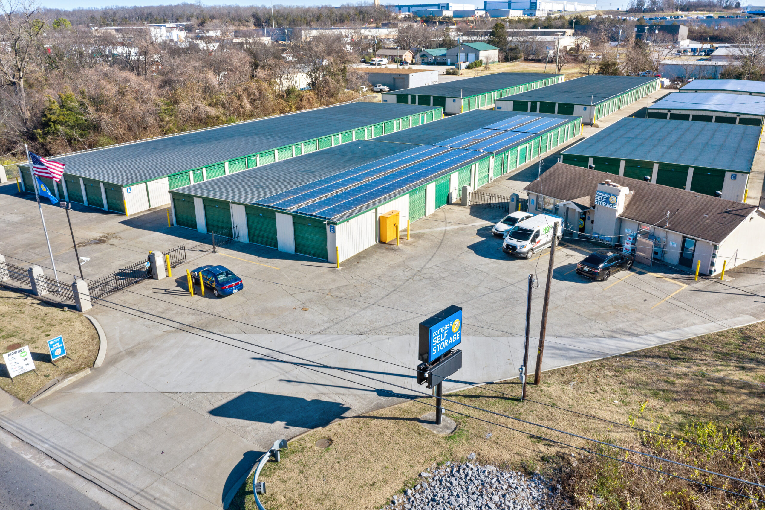 Aerial view of Compass Self Storage facility with rows of green storage units, solar panels, and office building.