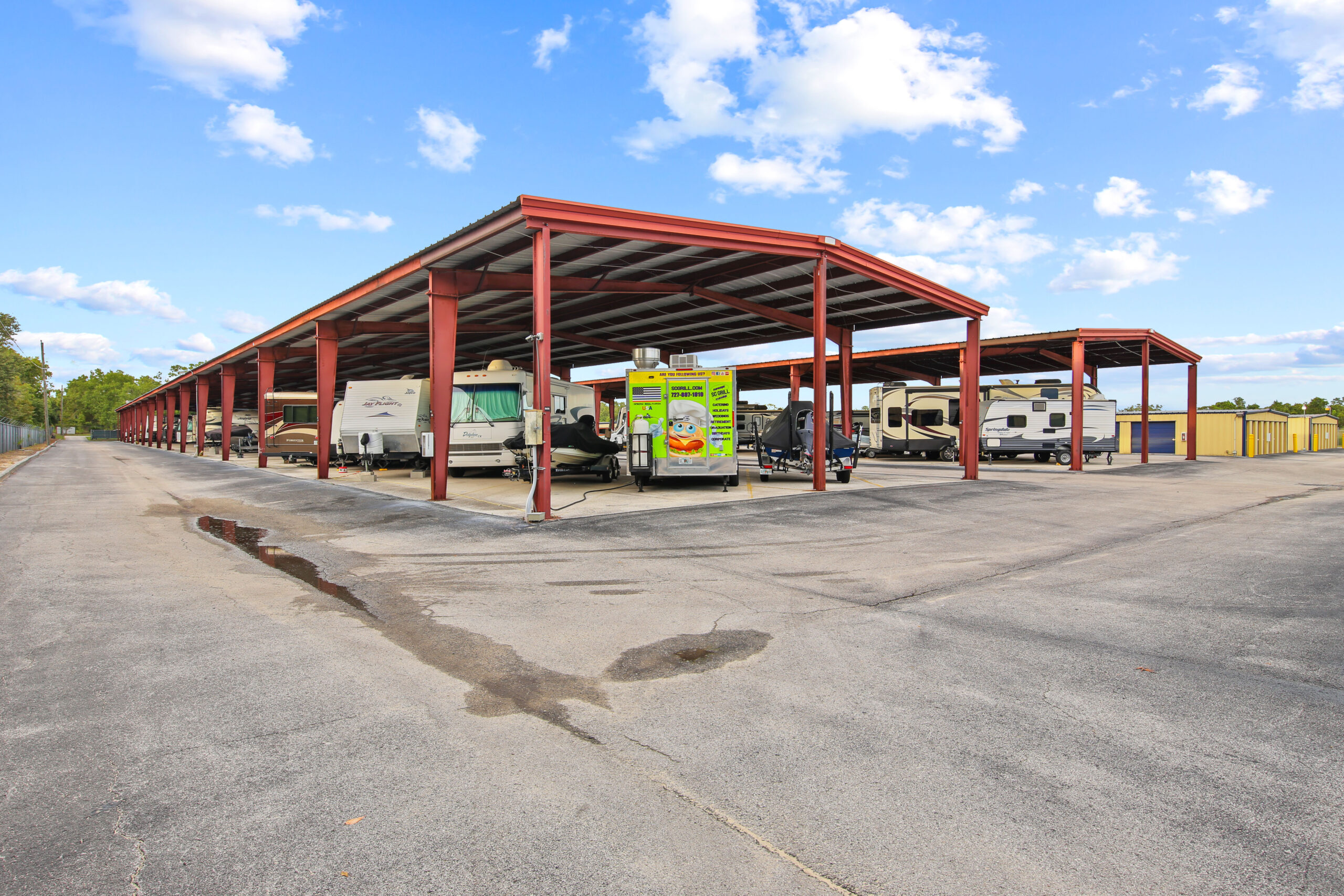 Covered RV, camper, and boat storage with yellow self-storage units under a blue sky.